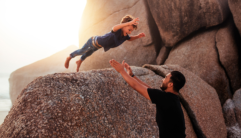 Child leaping off a boulder into his father's arms